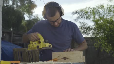 Young-male-woodworker-using-power-tools-to-plane-and-sand-lumber