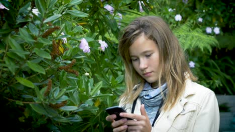 Una-Adolescente-Atractiva-Revisa-Los-Mensajes-De-Las-Redes-Sociales-En-Su-Teléfono-Inteligente-Sentada-En-El-Jardín-1