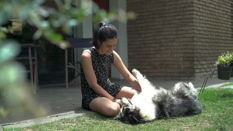 Young-Girl-Sit-and-Playing-with-Happy-Dog-Lying-on-the-Yard-Grass