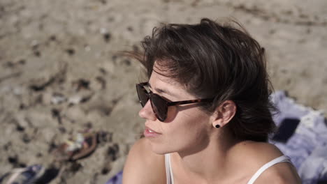 Young-brunette-women-sitting-on-beach-looking-at-view,-windswept-hair,-Gibraltar,-Spain