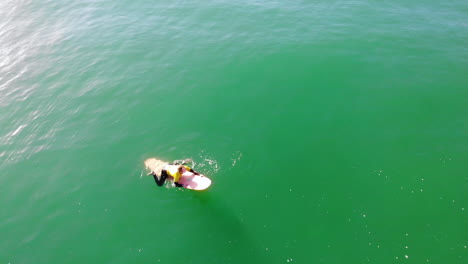 Surfer-Zander-Adelsohn-paddles-to-catch-a-wave-in-Pacific-Ocean-at-Huntington-Beach-in-surfing-competition-wearing-yellow-wetsuit-from-4k-aerial-drone