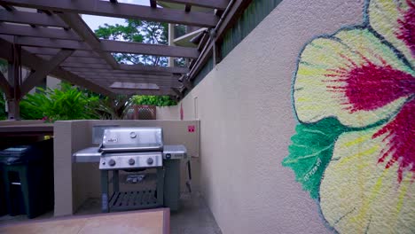 Decorated-wall-with-big-tropical-flower-on-summer-terrace-with-kitchen-equipment,-table-and-benches-on-a-vacation-residential-house