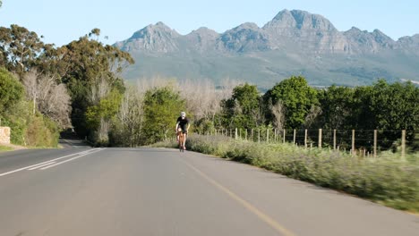 Amplia-Toma-De-Seguimiento-De-Un-Ciclista-De-Carretera-Masculino-Pedaleando-Lentamente-Cuesta-Arriba