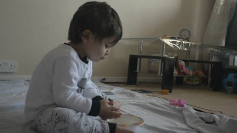 Small-child-with-brown-hair-eating-food-from-a-bowl-seated-on-the-living-room-floor