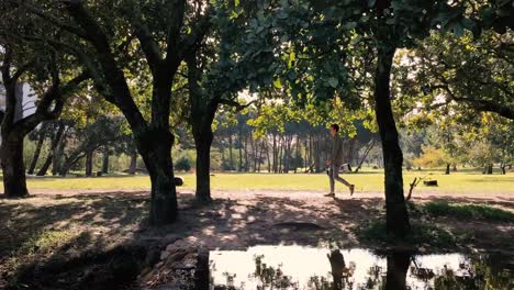 A-teenage-boy-walks-past-a-pond-in-a-park-holding-his-hover-board