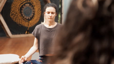 A-young-woman,-during-a-yoga-lesson,-closing-her-eyes-while-sitting-on-the-floor-and-repeating-a-position-following-the-teacher's-voice