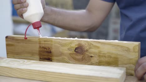 Close-up-shot-of-carpenter-craftsman-applying-wood-glue-to-a-2x4-wood-plank