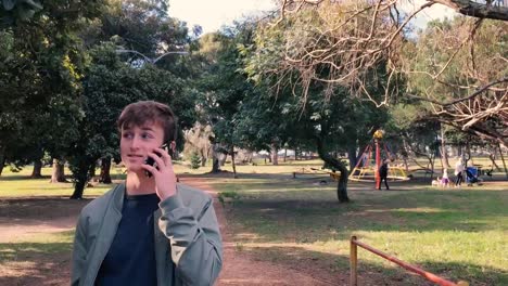 A-teenage-boy-walks-through-a-park-talking-on-his-mobile-phone