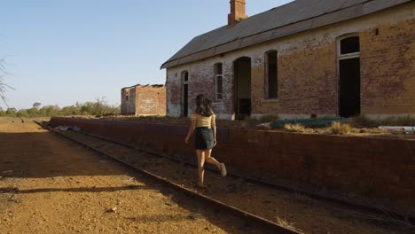 Una-Mujer-Joven-Caminando-Por-Las-Vías-De-Una-Antigua-Vía-Férrea-En-Un-Pueblo-Abandonado