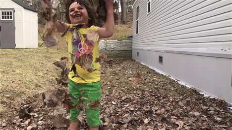 Slow-motion-shot-of-a-young-girl-joyfully-throwing-a-handful-of-leaves-into-the-air-and-watching-them-float-to-the-ground