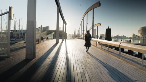 Stylish-girl-with-sunglasses-is-walking-into-the-sunrise-in-the-harbor-of-Barcelona-in-Spain