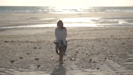 Young-women-walks-towards-camera-on-sandy-beach-at-sunset,-relaxing,-smiling,-happy