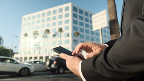 Ordering-a-Ride,-Businessman-Swiping-Through-App-on-Phone-in-Front-of-Busy-Corporate-Office