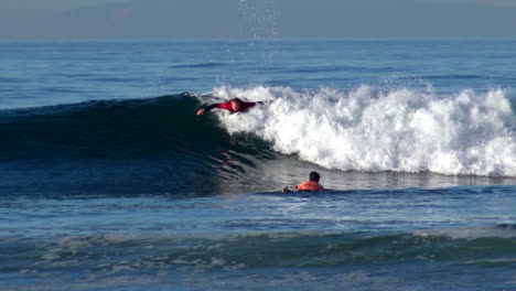 Surfer-Zander-Adelsohn-does-tricks---turns-in-Huntington-Beach-Pier-surfing-competition-on-short-board-in-Pacific-Ocean-waves-in-early-morning-wearing-red-wetsuit-rash-guard,-telephoto-lens-from-shore