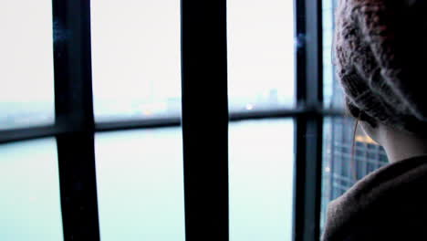 An-astonished-woman-looking-outside-an-elevator-with-transparent-glass-walls,-during-a-ride-to-the-top-of-a-skyscraper