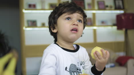 Young-child-little-boy-eats-a-fresh-apple-and-picks-up-an-orange-slider-shot