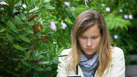 Attraktives-Teenager-Mädchen-überprüft-Social-Media-Nachrichten-Auf-Ihrem-Smartphone,-Das-Im-Garten-Sitzt