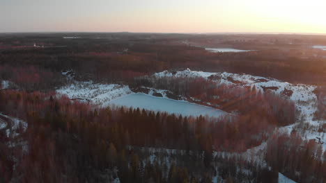 Aerial,-tilt-down,-drone-shot,-towards-a-old-closed-Hammaslahti-copper-mine,-surrounded-by-snowy-and-leafless-forest,-on-a-spring-day,-in-Joensuu,-North-Karelia,-Finland