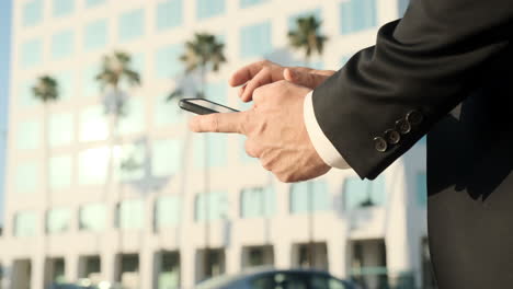 California-Corporate-Businessman-Pulls-Phone-out-of-Pocket-to-Text,-Palm-Trees-and-Office-Building-in-Background