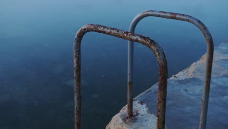 Escaleras-Oxidadas-En-Una-Piscina-Al-Aire-Libre,-En-La-Costa-De-Guernsey,-Al-Atardecer