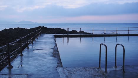 Landscape-view-of-an-outdoor-swimming-pool,-in-the-coastline-of-Guernsey,-at-dusk