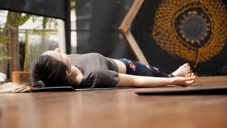 A-young-woman-lying-on-the-floor-during-a-yoga-lesson,-learning-a-meditation-technique-involving-breathing