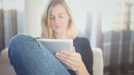 A-woman,-sitting-on-the-couch,-reading-something-on-a-web-connected-tablet