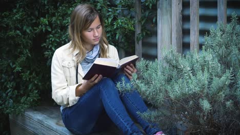 Attractive-teenage-girl-reads-book-in-the-patio-among-plants-1