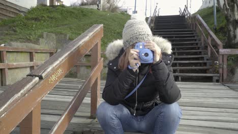 Junge-Frau-Macht-Ein-Foto-Mit-Einer-Sofortbildkamera,-Die-Auf-Einer-Holztreppe-Sitzt