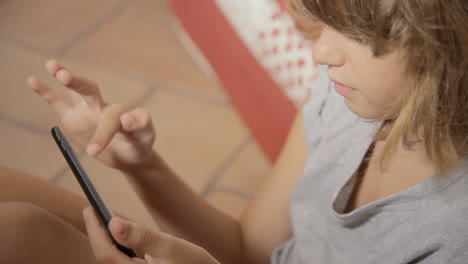 A-cute-little-girl-sitting-on-the-floor-and-touching-her-smartphone,-looking-interested