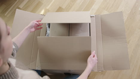 Over-the-shoulder-shot-of-female-person-opening-postal-parcel-with-redundant-packaging