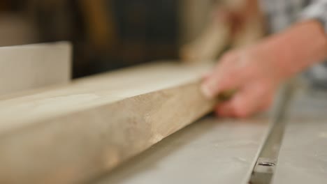 Wooden-plank-with-bark-pushed-through-table-saw-by-experienced-hand