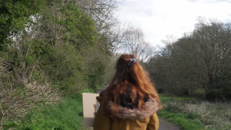 Young-woman-with-notes-in-her-hands-walks-over-a-path-between-trees-on-a-nature-trail,-looks-around-and-orientates-herself