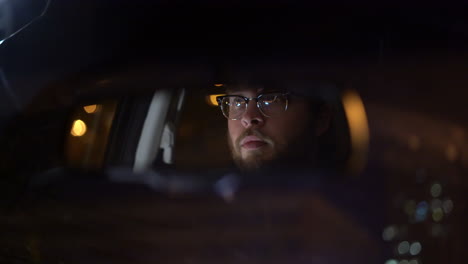 4K-footage-of-man-looking-into-his-rearview-mirror-in-his-car-driving-at-night