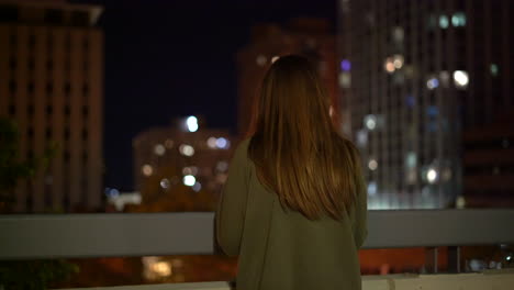 Imágenes-De-4k-De-Mujer-Con-Vistas-A-Una-Ciudad-Por-La-Noche-Con-Luces-Y-Rascacielos-En-El-Fondo