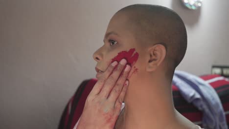 Bald-Cancer-patient-Indian-girl-applies-color-powder-on-cheeks-on-Holi,-Indian-festival-at-home-due-to-covid-19-lockdown-and-smiles