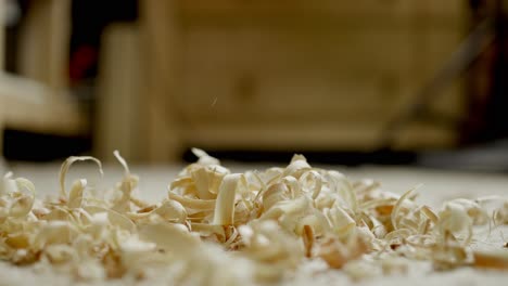 Wood-chips-falling-to-the-ground,-forming-a-small-pile-of-wood-residue-before-blurry-background-in-carpenter's-workshop