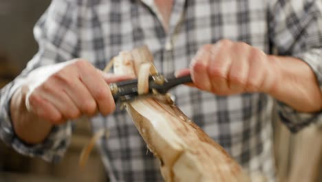 Two-handed-plane-scrapes-shavings-off-of-wooden-workpiece-in-carpenter's-workshop