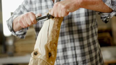 Carpenter-in-checked-shirt-planing-large-round-wooden-stick-with-two-handed-hand-plane