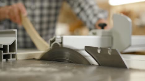 Joiner-uses-circular-bench-saw-to-cut-long-latch-into-same-length-quadratic-pieces,-close-up-slow-motion