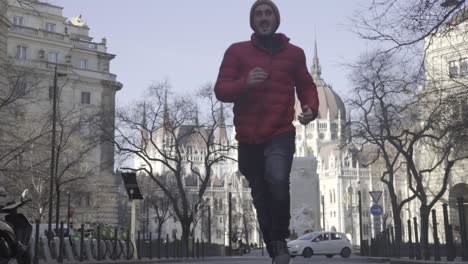 Man-running-and-jumping-in-front-of-the-Budapest-Parliament,-Europe,-slow-motion,-low-angle