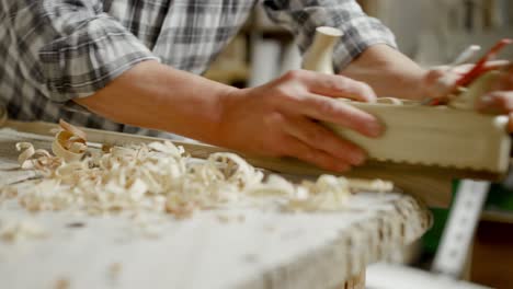 El-Hombre-Con-Camisa-A-Cuadros-Usa-Un-Plano-De-Mano-Para-Cortar-Una-Capa-Delgada-De-Madera-Del-Listón