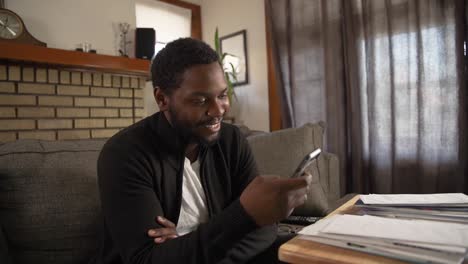 Black-man-texting-on-phone-smiling-in-living-room-medium-shot