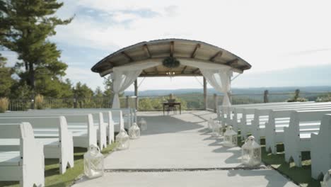 Walking-down-the-isle-of-a-beautiful-outdoor-wedding-ceremony-venue-with-the-Gatineau-Hills-and-a-sunny-cloud-filled-blue-sky-in-the-background-at-Le-BelvÃ©dÃ¨re-in-Wakefield,-Quebec,-Canada