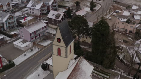 High-tower-of-a-christian-church-in-a-quite-village-near-Lake-Walensee-in-Switserland-on-a-cold-winter-day-when-snow-is-falling-down