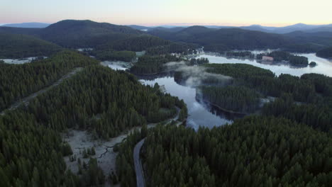 Acercándose-Desde-El-Aire-A-Un-Lago-De-Montaña-Brumoso-Rodeado-De-Bosques-De-Coníferas