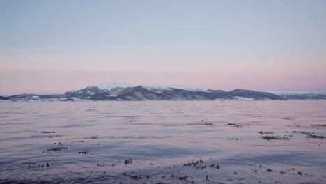 Winter-Sunset-Over-Rippling-Fjord-With-Snowcapped-Mountain-In-Background