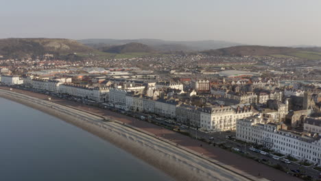 Aerial-view-flying-over-Llandudno-seafront-and-beach-as-the-sun-begins-to-set-over-the-town,-Llandudno,-North-Wales,-UK