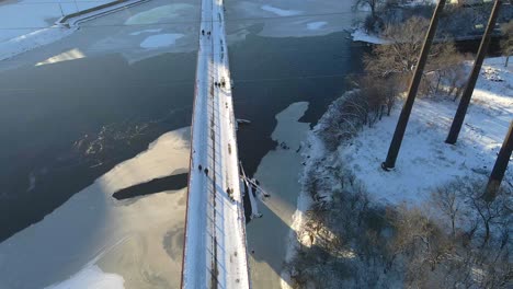 Aerial-view-of-people-at-stone-arch-bridge-crossing-the-mississippi-river-in-Minneapolis-winter-afternoon-ice-formations