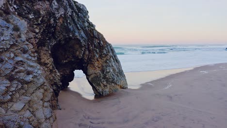 Aerial-Drone-View-of-Lisbon-Beach-with-Arch-Rock-Formation,-on-the-Portugal-Coast-by-Sintra-at-Praia-da-Adraga,-a-Beautiful-Sandy-Beach-on-the-Atlantic-Ocean